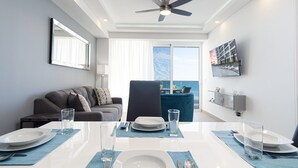 A modern dining area with a table set for four, a sofa, and a view of the ocean through large windows.