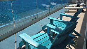 Ein Balkon mit türkisfarbenen Stühlen und einem Tisch mit Blick auf einen Strand.