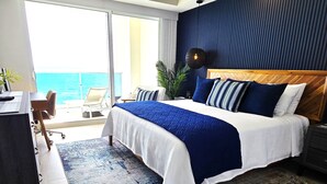 Ein modernes Schlafzimmer mit einem großen Bett, einem Schreibtisch und Blick auf den Ozean.