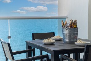 A balcony table with a metal bucket containing bottles and ice, two bowls of popcorn, and a chair.