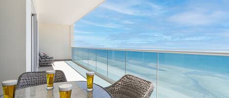 Un balcon avec une table en verre et des chaises en osier, donnant sur une plage.