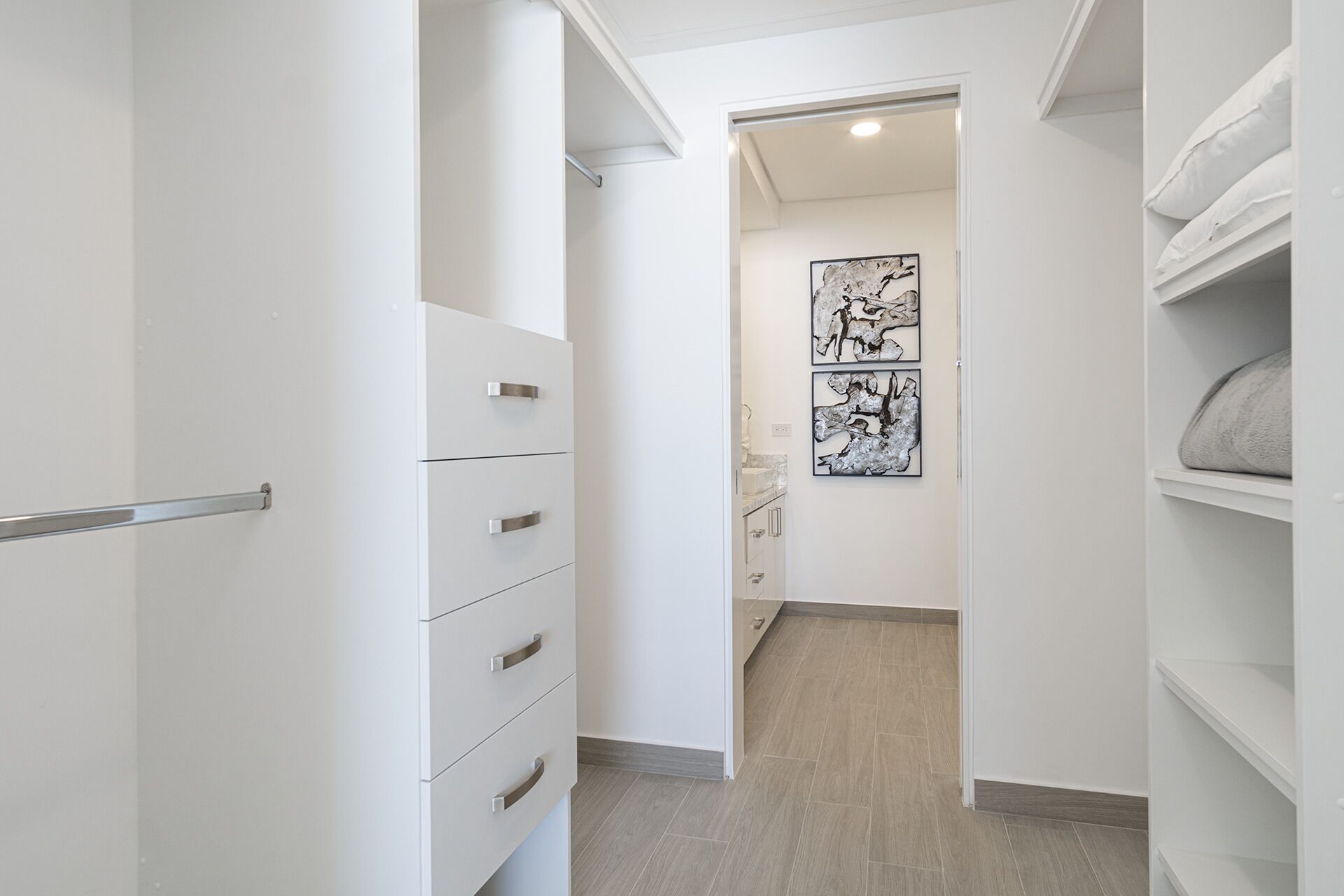 Un couloir étroit doté de meubles blancs, d’une main courante en métal et d’une porte donnant accès à une salle de bain.