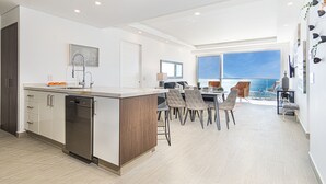A modern kitchen with a central island, a dining area with chairs, and a large window offering a view. - Amazing 2 bedroom Beach Front Condominium at Encantame C1102 (Puerto Peñasco)