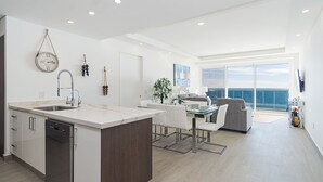 Una cucina moderna con isola centrale, zona pranzo con tavolo in vetro e vista sul mare attraverso ampie finestre.