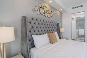 Ein Schlafzimmer mit einer gesteppten Kopfstütze, weißer Bettwäsche und einem dekorativen Wandbild.