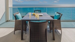 Un balcone con tavolo e sedie, vista su una piscina e il mare.