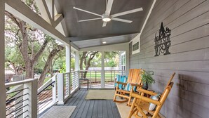 Une véranda couverte avec un ventilateur de plafond, des fauteuils à bascule en bois et une vue sur le jardin arrière.
