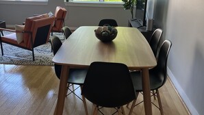 Un coin repas avec une table en bois, des chaises noires et un bol rempli d’objets décoratifs.