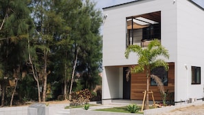 Ein modernes, zweistöckiges Gebäude mit flachem Dach, großen Fenstern und einer Fassade aus weißem Putz und Holz.