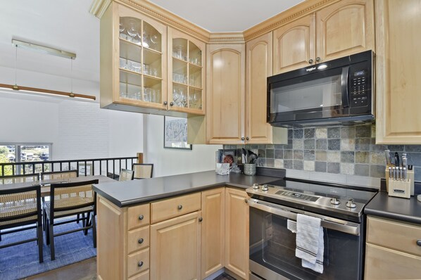 A kitchen with wooden cabinets, a microwave, an oven, and a dining area with a table and chairs.