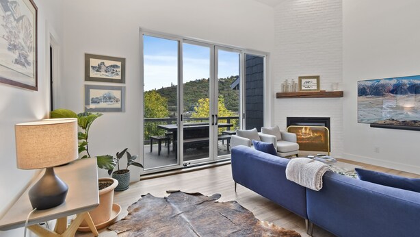 A modern living room with a blue sofa, a fireplace, and a large sliding glass door leading to a balcony. - 3BR home central to Main Street and hiking trails, with private firepit, hot tub & balcony (Park City)