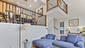 A modern living room with a blue sectional sofa, a glass coffee table, and a staircase with wooden railings. - 3BR home central to Main Street and hiking trails, with private firepit, hot tub & balcony (Park City)