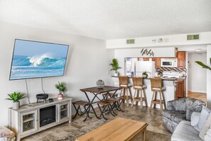 Sala de estar com televisão, área de jantar, cozinha e assentos.