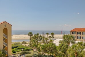 A coastal hotel with a view of the beach, palm trees, and a flag.