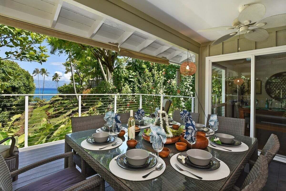 A dining area with a table set for four, overlooking a lush garden and the ocean.