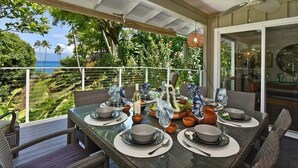 Un comedor con una mesa lista para cuatro personas, con vistas a un jardín exuberante y el océano.
