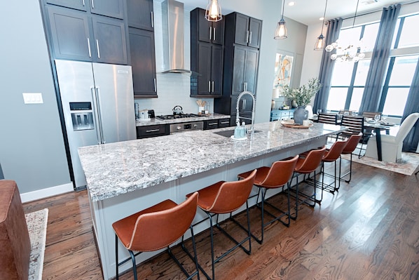 A modern kitchen with dark cabinets, a stainless steel refrigerator, a granite countertop, and a bar area with stools.