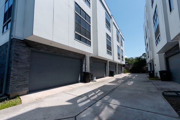 A modern residential building with multiple garage doors, a clean concrete driveway, and a clear sky. - Rooftop ❤︎ EastDWTN ★ Sleeps 6 + FREE Parking (Houston)