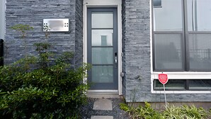 Un bâtiment moderne avec une façade en pierre grise, une porte grise dotée d’un panneau de verre et une fenêtre sur laquelle est apposée une enseigne rouge.