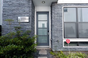 A modern building with a grey stone facade, a grey door with a glass panel, and a window with a red sign.