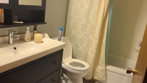 Un bagno con lavandino bianco, mobile contenitore scuro, wc e zona doccia.