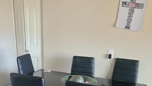 Una sala conferenze con un tavolo in vetro, quattro sedie nere e un poster appeso al muro.