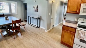 Une cuisine spacieuse avec des meubles en bois, une table à manger avec des chaises et une vue sur l’extérieur par une fenêtre.