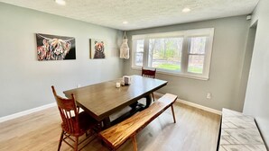 Un vaste espace dédié à la salle à manger, avec une grande table en bois, deux chaises et un banc. Deux tableaux sont accrochés au mur, et un luminaire est suspendu au plafond.
