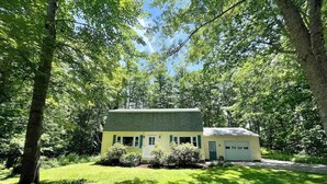 Une maison de plain-pied dotée d’un toit végétalisé et d’un garage, entourée d’une végétation luxuriante et d’arbres.
