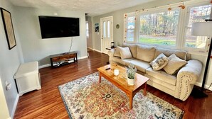 Un salon avec un téléviseur à écran plat, une table basse en bois, un canapé beige et un tapis à motifs.