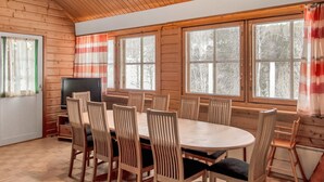 A wooden-paneled room with a round table and chairs, a television, and large windows with blinds.