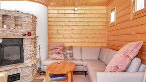 A cozy living room with a stone fireplace, wooden ceiling, and a grey sofa with pink cushions.