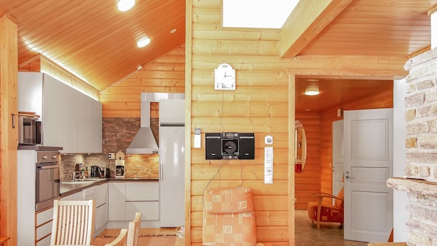 A cozy cabin-style kitchen with wooden walls, a dining area with a table and chairs, and a stone wall.