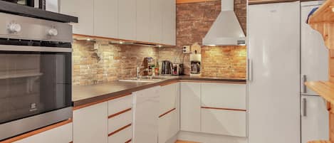 A modern kitchen with white cabinetry, a built-in oven, a coffee maker, and a brick wall backsplash.