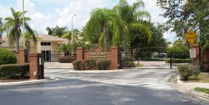 A gated entrance to Sun Lake Condominiums with a brick gate, palm trees, and a clear sky.