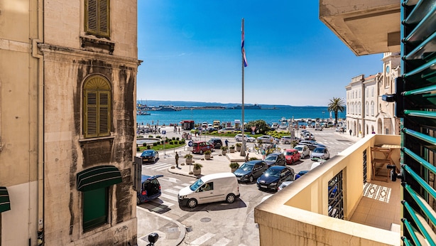 A view of a street with parked cars and a flagpole with a flag. - Riva City Rooms (Split)