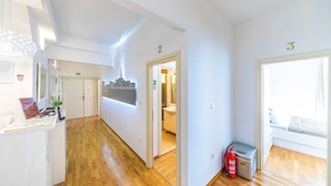 A hallway with wooden flooring, a reception desk, and numbered doors leading to rooms. - Riva City Rooms (Split)