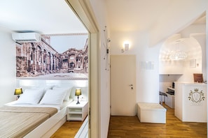 A hotel room with a bed, bedside tables, a desk, and a view of a cityscape through a window. - Riva City Rooms (Split)