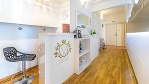 A reception area with a modern bar stool, a reception desk with a logo, and a hallway leading to a door. - Riva City Rooms (Split)