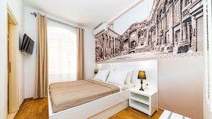 A modern bedroom with a bed, bedside table, and a wall mural. - Riva City Rooms (Split)