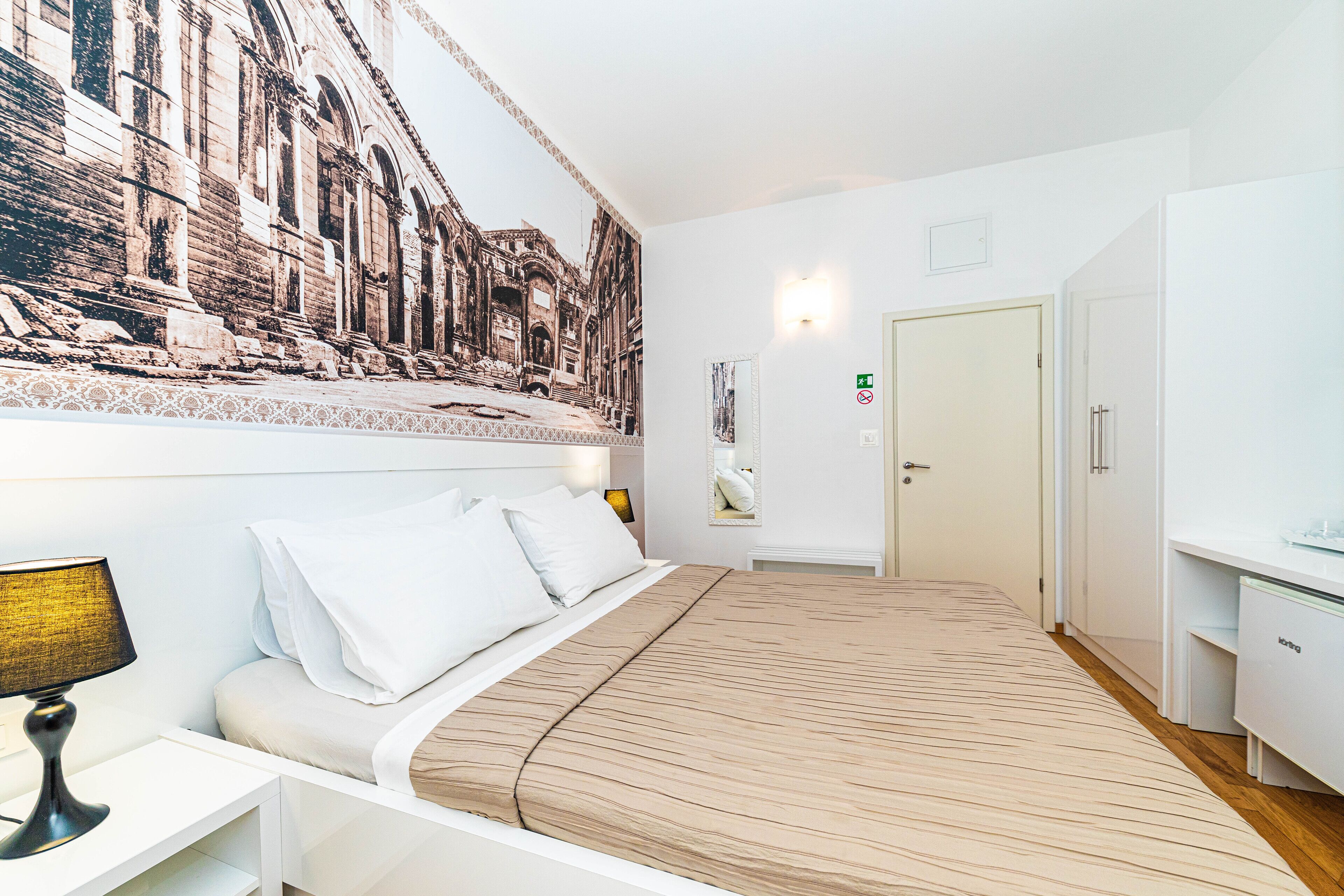 Una habitación de hotel con una cama grande, una mesita de noche, un escritorio y un espejo montado en la pared.