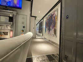 Un pasillo con diseño moderno, que incluye un banco blanco, un televisor montado en la pared y un cuadro abstracto grande.