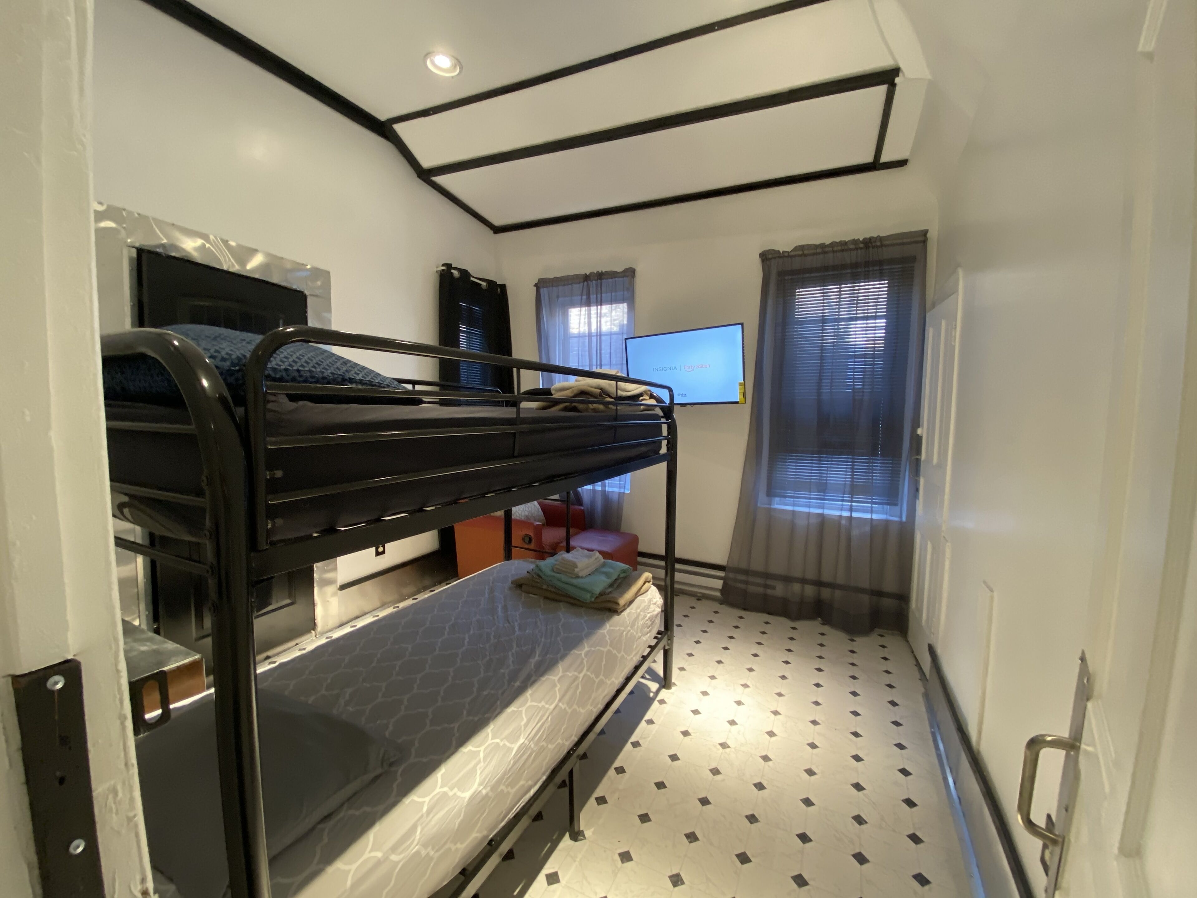 Habitación pequeña con literas, televisión y ventana con cortinas.