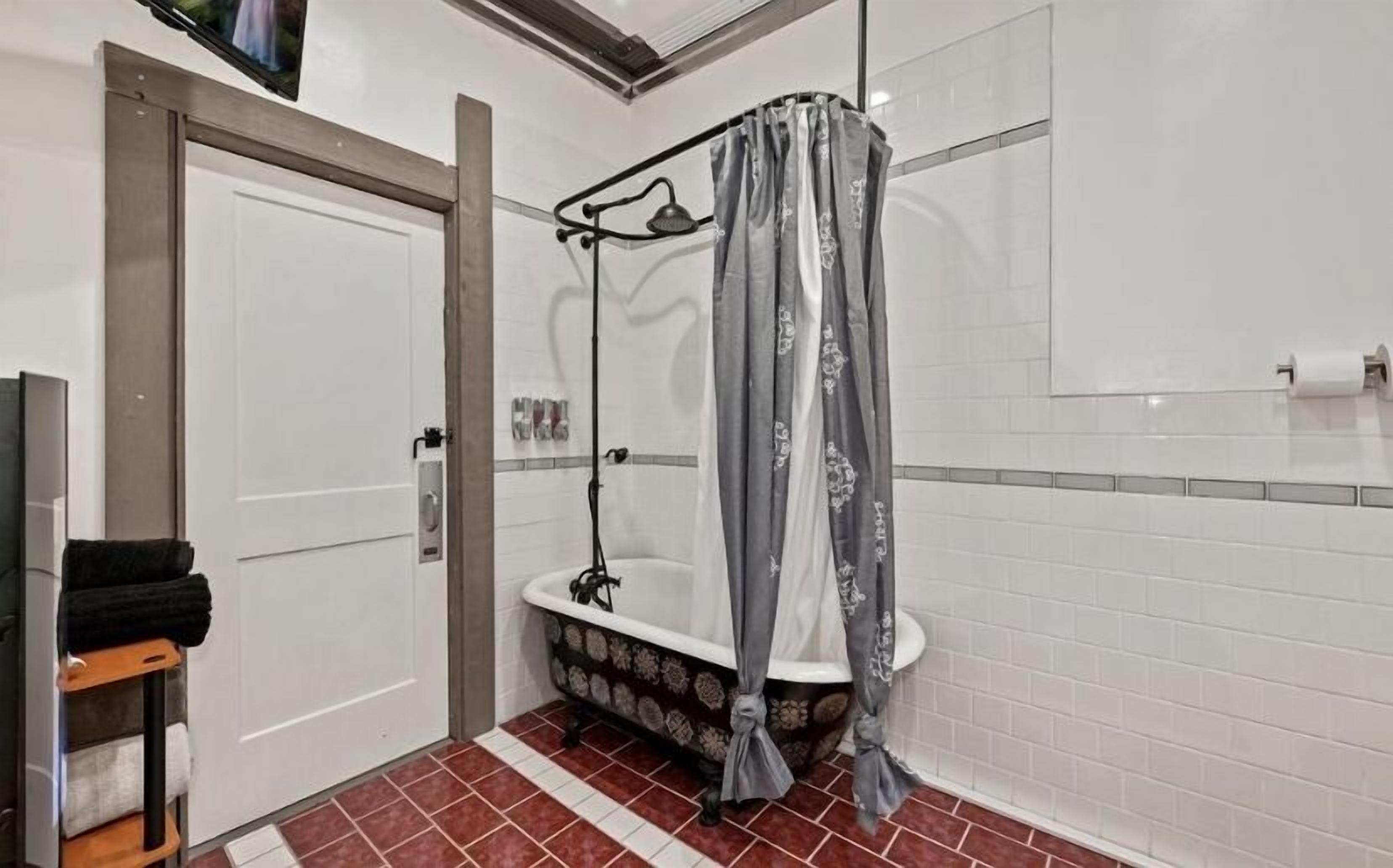 A bathroom with a shower, white tiled walls, a door, and a tiled floor.