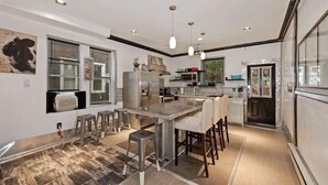 Een moderne keuken met een centraal eiland, roestvrijstalen apparatuur en hangende verlichting.