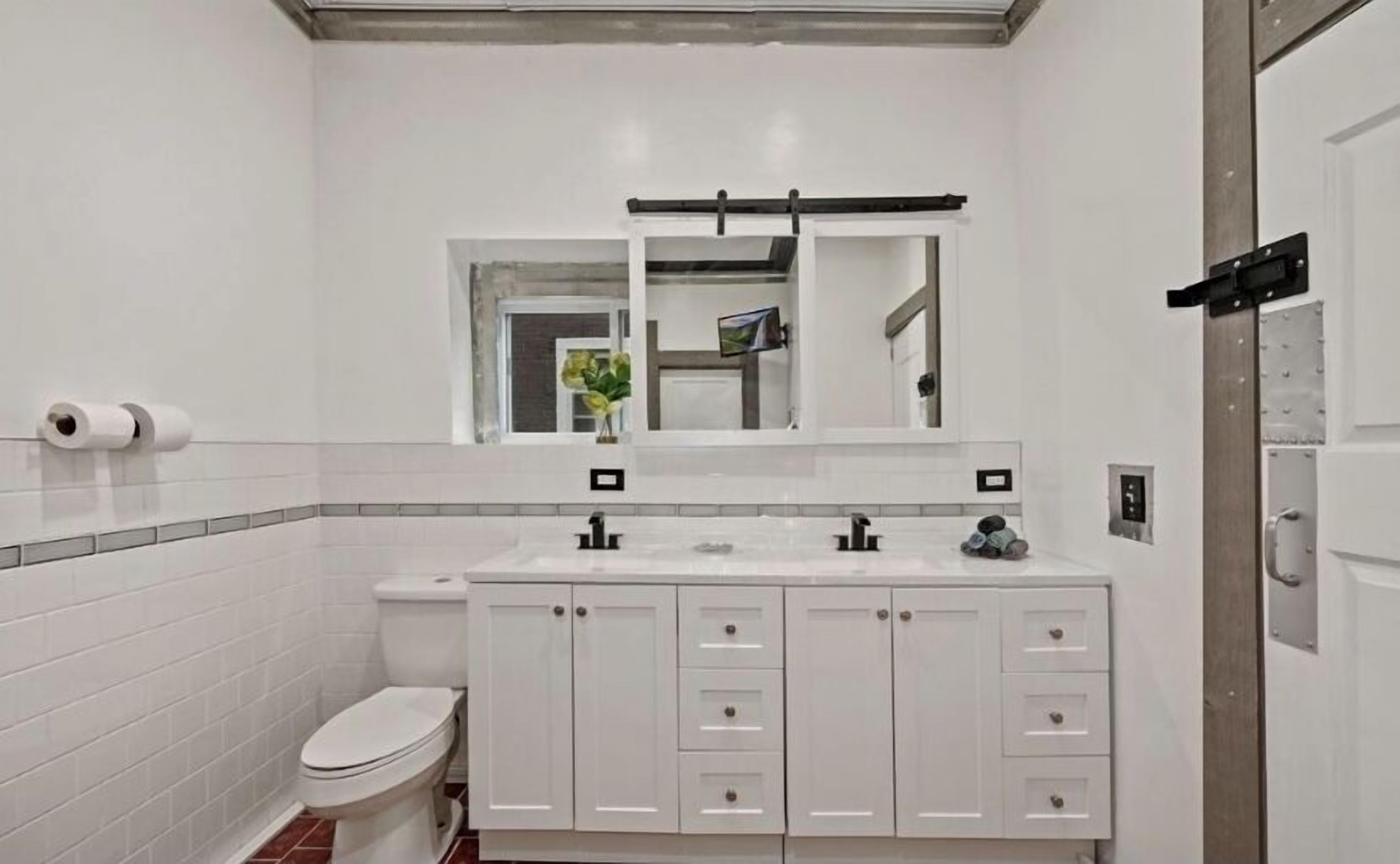 A modern bathroom with a white toilet, a sink with a mirror above, and cabinets below.