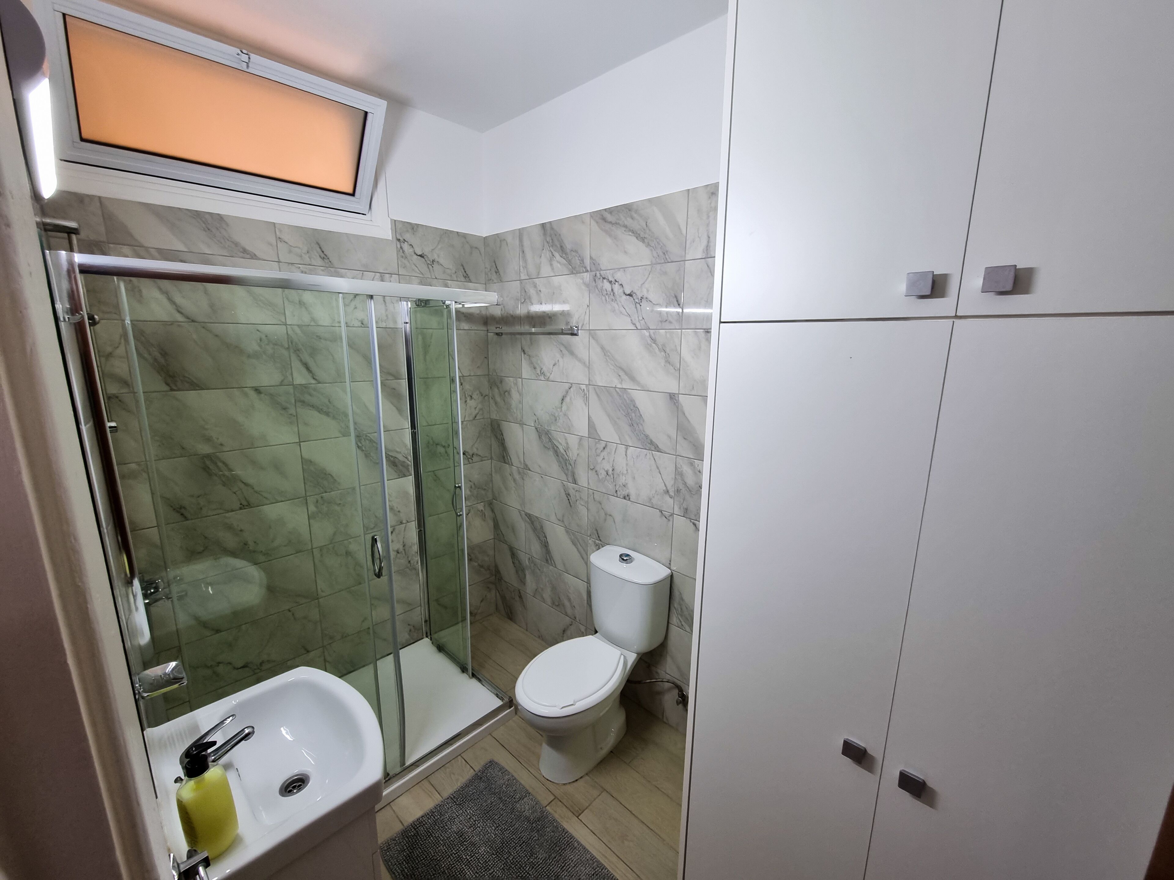 A modern bathroom with a glass-enclosed shower, a white toilet, and a sink with a soap dispenser.