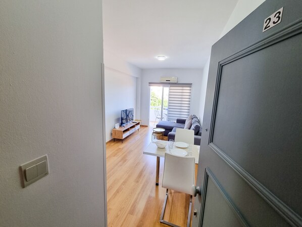 A modern living room with a flat-screen TV, a dining table with chairs, and a sofa. - Springfield Park Apartment (Larnaca)
