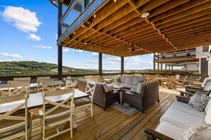 Une terrasse extérieure avec un plancher en bois, des meubles en osier et une vue sur un lac et des collines.