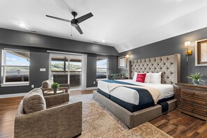 A bedroom with a large bed, a ceiling fan, and a view of the outdoors.